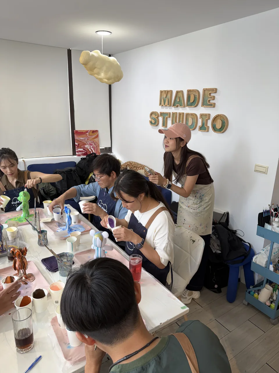 MADE STUDIOの文字壁の前で、テーブルを囲んでフルイドベア作りに集中する同僚たち