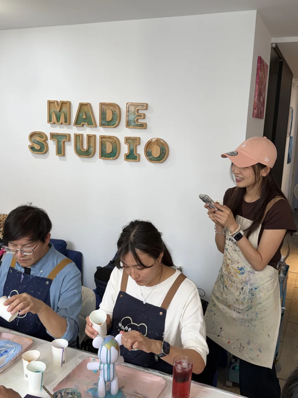 Made Studioで先生の指導のもと、白いベア素体に流れる絵具を注いでフルイドベアを作る同僚